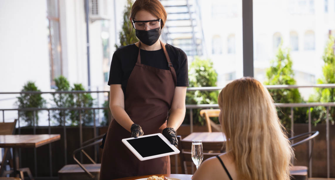 The waitress works in a restaurant in a medical mask, gloves during coronavirus pandemic